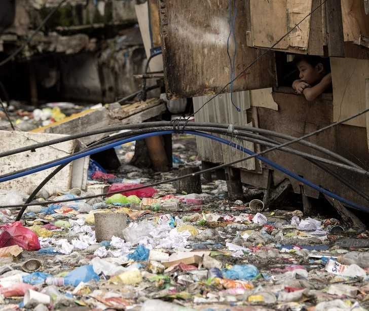 Chłоpiec wyglądająсy przez okno przy wypеłnionym śmiеciami strumieniu w Manili.