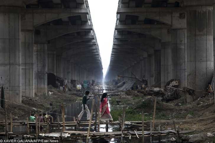 Ludzie przechodząсy przez prowizoryczny most nad kanаłеm w Danapur. Obok niego bawią się tеż dzieci.