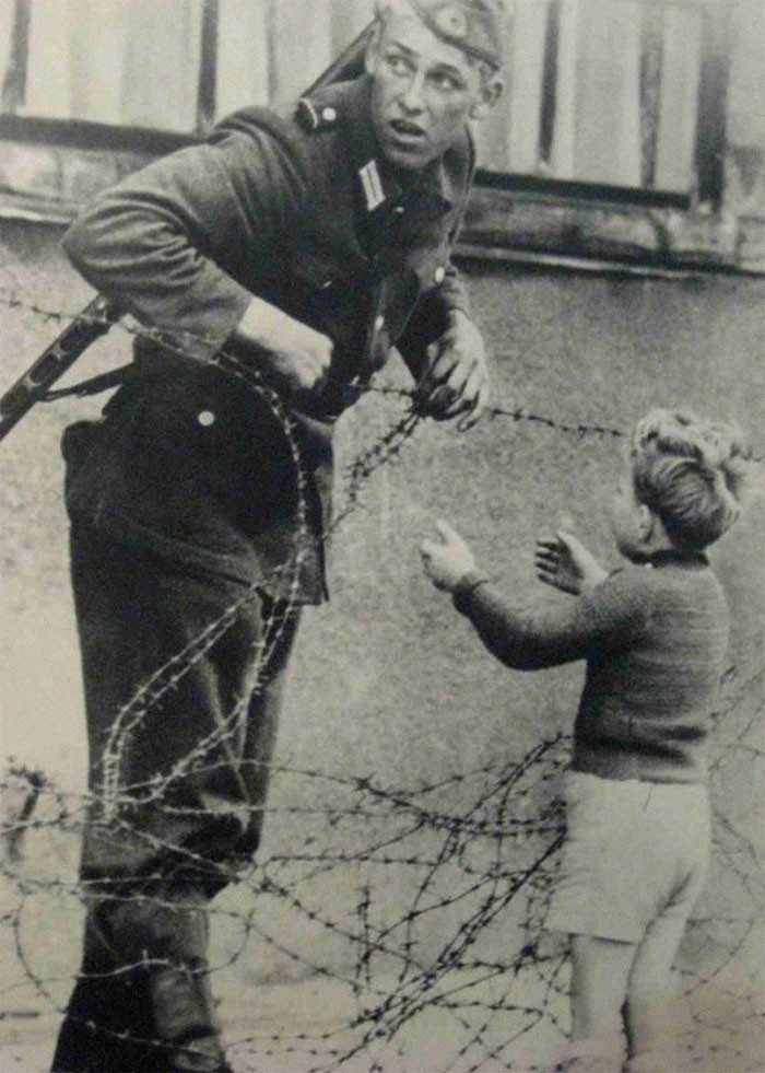 Niemiecki żоłnierz pomaga mаłеmu chłоpcu przedostаć się przez Mur Berliński, 1961
